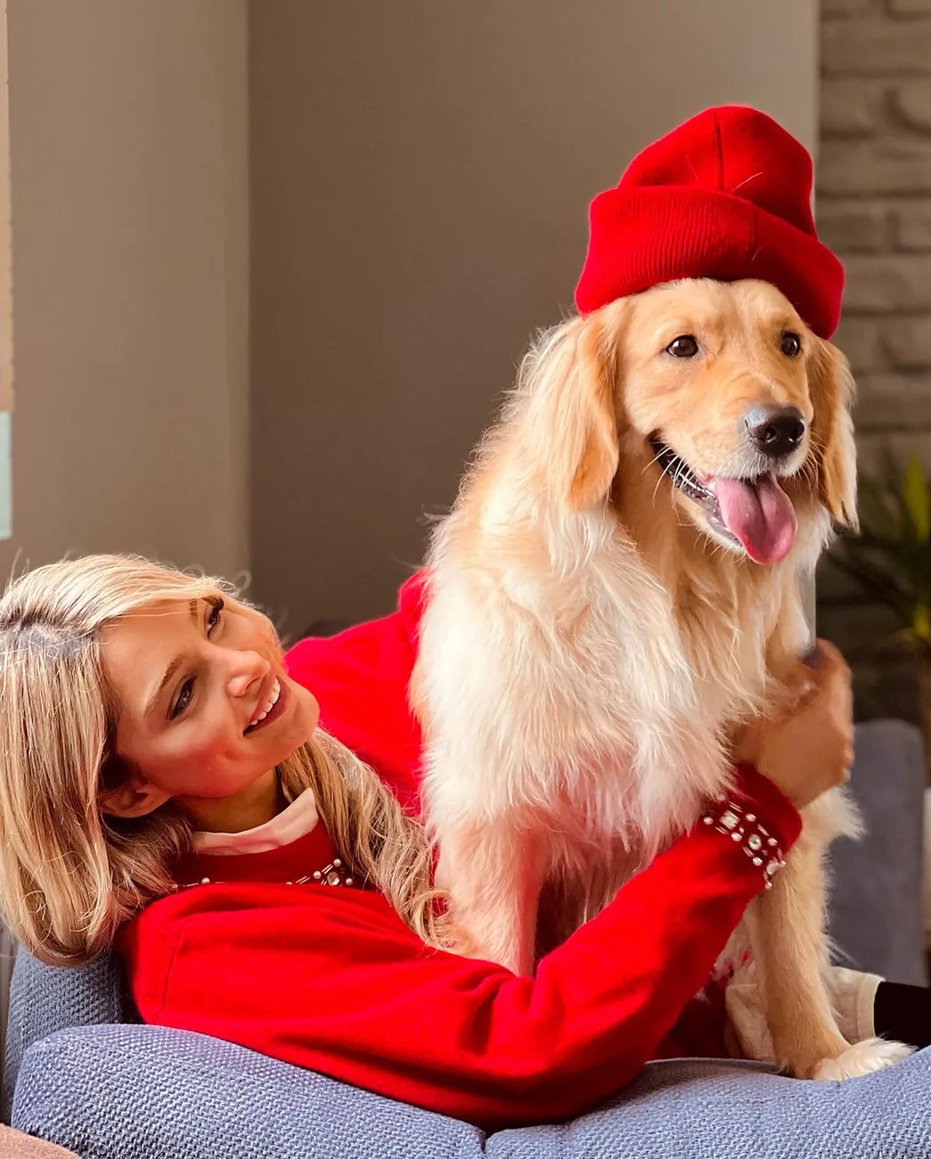 A dog sitter in a red sweater cuddling a golden retriever indoors